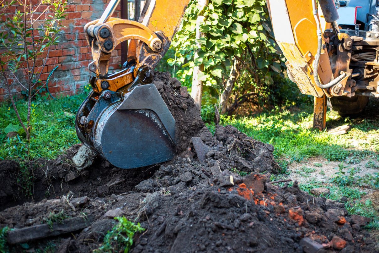 excavator-digs-ground-with-large-bucket-land-plot-lay-water-supply-system Excavator digging a yard to lay new drainage pipe