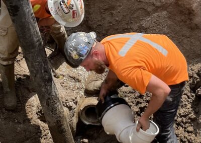 Two construction workers performing a sewer line repair inside an excavation trench.