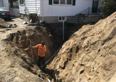 Construction worker in a trench alongside a residential home, performing underground pipe installation or repair.