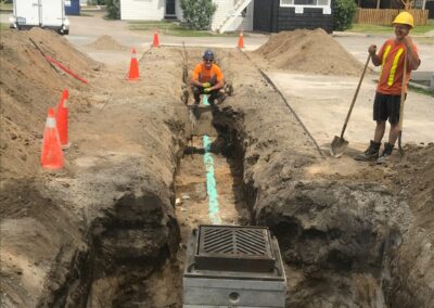 Two construction workers installing or repairing an underground sewer or drainage system in a roadway.