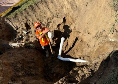Construction worker standing in a deep excavation trench, working on underground piping.